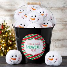 a bucket filled with snowballs sitting on top of a table next to a christmas tree