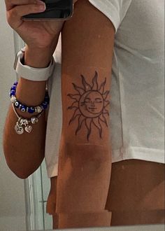 a woman is taking a selfie with her cell phone and sun tattoo on her arm