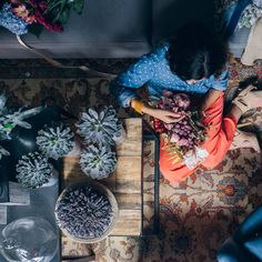 an overhead view of a woman arranging flowers on a table with other plants and vases