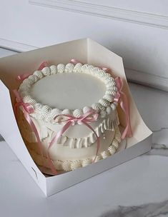 a white cake in a box with pink ribbon around it on a marble countertop