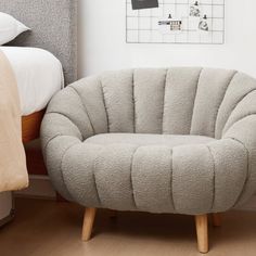 a grey chair sitting next to a bed in a room with white walls and wooden floors