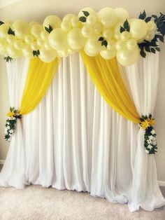 a white curtain with yellow drapes and flowers on the side is decorated with balloons