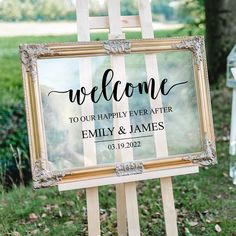 a welcome sign sitting on top of a easel in front of a grass covered field