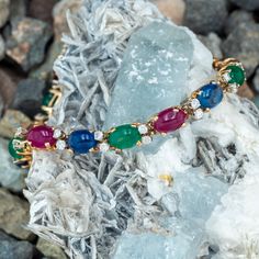 This vibrant bracelet is four-prong set with six (6) oval sapphire cabochons, five (5) oval emerald cabochons and six (6) oval ruby cabochons. The cabochons alternate with two (2) four-prong set, round brilliant cut diamonds. The bracelet measures 6.1mm wide, rises 5.6mm above the wrist by 7.5 inches long, finished with a hidden box clasp and figure eight safety. One of the emerald is lightly chipped but this does not distract from the beauty of this bracelet. It is crafted in 14K gold with a light rich patina. Multi Gemstone Bracelet, Box Clasp, Round Brilliant Cut Diamond, Gemstone Bracelet, Brilliant Cut Diamond, Round Brilliant, Prong Setting, Yellow White, Diamond Cuts