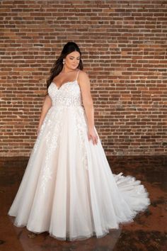 a woman standing in front of a brick wall wearing a wedding dress with flowers on it