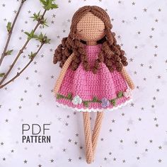 a crocheted doll with brown hair and pink dress sitting on a white surface