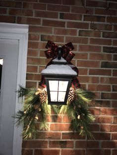 a christmas wreath hanging from the side of a brick wall next to a lit lantern