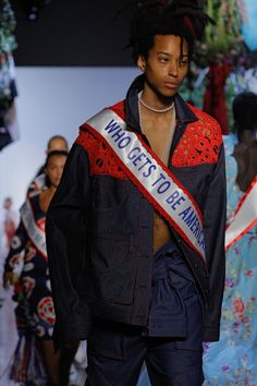 a man with dreadlocks walks down the runway wearing a sash that says who gets to be married?