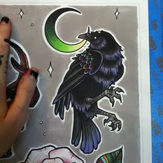 a drawing of a black bird sitting on top of a piece of paper with the moon and crescent above it