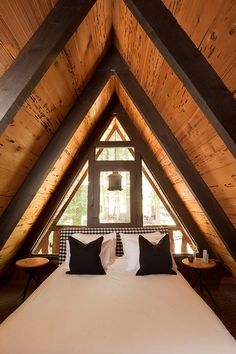 a bed in a loft with wooden walls and ceiling beams, topped by black and white pillows