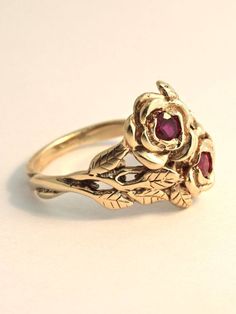 Two detailed roses make up this elegant ring, their stems entwining and forming the band. The ring is cast in solid 14K gold and two 3 mm rubies are set in the center of each rose. Indulge yourself or someone special in this sparkling bouquet. We will contact you to let you know if we have your chosen ring size in stock or when to expect shipment. All Marty Magic Jewelry is packaged in a beautiful ring box embossed with the gold foil Marty Magic dragon logo. Perfect for any occasion! Designed in Formal Rose Colored Flower Shaped Rings, Vintage 14k Gold Flower Promise Ring, Formal Flower Shaped Rings With Rose Design, Vintage Rose Gold Ruby Wedding Ring, Vintage 14k Gold Flower Ring For Formal Occasions, Vintage Rose Gold Ruby Promise Ring, Vintage 14k Gold Flower Ring For Anniversary, Vintage Flower Rings For Formal Occasions, Formal Rose Flower Shaped Rings