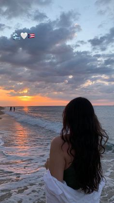 a woman standing on top of a sandy beach next to the ocean at sunset with people in the background