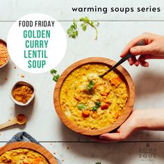 a person holding a wooden bowl filled with curry next to other bowls and spoons