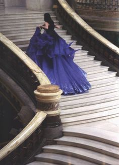 a woman in a blue dress walking down some stairs