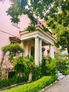 a pink building with white pillars and columns on the front, surrounded by greenery