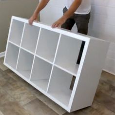 a man standing next to a white bookcase on top of a hard wood floor