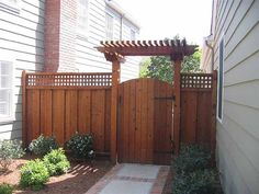 a wooden gate in the middle of a yard with landscaping around it and brick walkway