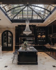 an elegant kitchen with black cabinets and marble flooring is featured in this image, the center island has a chandelier that hangs over it