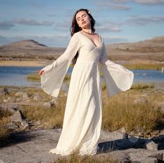 a woman in a white dress is standing on some rocks and looking off into the distance