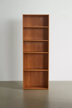 a wooden bookcase sitting on top of a cement floor next to a white wall