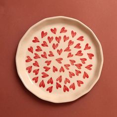 a white plate with red hearts painted on the inside of it, sitting on a pink surface