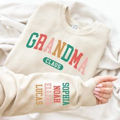 "the perfect Christmas gift for the beloved Grandma Claus in your life! This unique Grandma sweater is not only cozy, but can also be personalized to include the names of her precious grandkids. HOW TO ORDER: 1- Please check all of the photos. 2- Select your T-shirt size from selection box. 3- Select your T-shirt color from the selection box. 4- Personalization box is only for design color information, enter your design or text color in the personalization box (see images for options). 5- Select the quantity. 6- Go to add to cart. 7- Complete checkout!  SWEATSHIRT DETAILS: * 50% Cotton - 50% Polyester * 1x1 ribbed collar, cuffs and waistband with spandex * Set-in sleeves * UNISEX SIZING, not a Women's size! * Brands of Sweatshirts we use, but are not limited to, are Gildan, Jerzees, Hanes. Gifts For Nana, Custom Embroidered Sweatshirt, Sweatshirt Details, Grandma Sweater, Personalized Grandma, Nana Gifts, Sweatshirt Christmas, Cozy Fits, Embroidered Sweatshirts