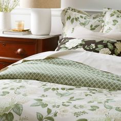 a bed with green and white floral comforter on top of it next to a night stand