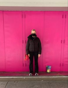 a person standing in front of a pink wall wearing a face mask and black pants