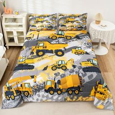 a bed with yellow construction trucks on it and white nightstands in the background,