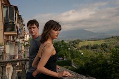 a man and woman standing next to each other on top of a stone wall in front of a building