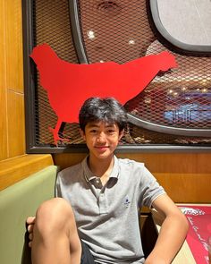 a young boy sitting in front of a red bird