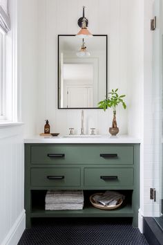 a bathroom with white walls and green drawers, black flooring and a large mirror above the sink