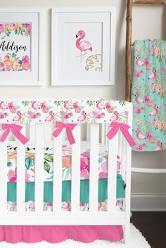 a white crib with pink and green bedding in the corner next to two framed pictures