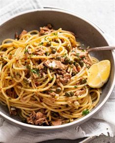 a bowl filled with pasta and meat on top of a white cloth next to a fork