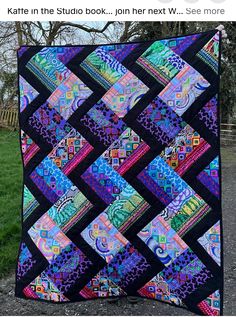 a colorful quilt hanging from the side of a tree in front of some grass and trees