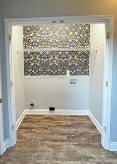 an empty room with wood flooring and wallpaper on the walls, looking into another room