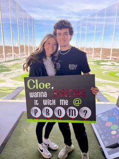 a man and woman standing next to each other holding a sign that says cloe wanna swing it which me prom?