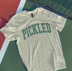 a t - shirt that says pickled on it sitting next to a tennis net