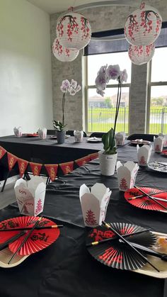 a black table topped with red and white paper fans next to vases filled with flowers