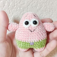 a small pink and green stuffed animal in someone's hand