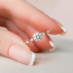 a woman's hand with a diamond ring on her finger and white manicured nails