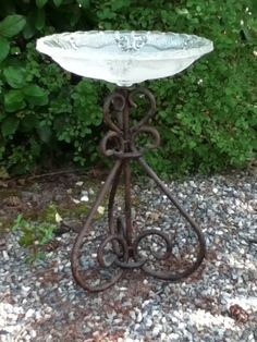 an iron stand with a glass bowl on it in front of some bushes and rocks