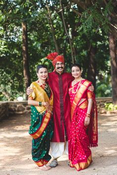 two people standing next to each other in colorful sari and headgear, with trees in the background