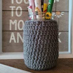 a crocheted jar with pens, pencils and other items in it sitting on a shelf