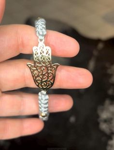 a hand holding a silver and gold hamsa necklace with filigreet on it