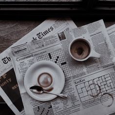 two cups of coffee are on top of newspapers with spoons and napkins next to them