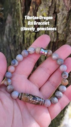 a person holding a beaded bracelet in their left hand near a tree trunk with water running down it