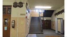 an empty hallway with stairs leading up to the door and two clocks on the wall