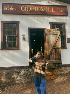 a woman drinking from a bottle in front of a white building with wooden shutters