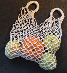 a white net bag filled with fruit on top of a black table next to an orange and green apple